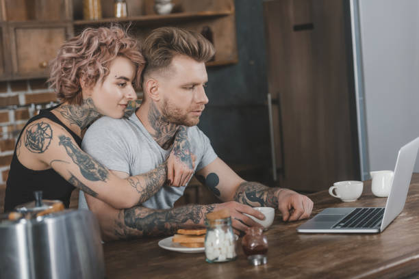 istock tattooed couple hugging and using laptop during breakfast in kitchen 917252040