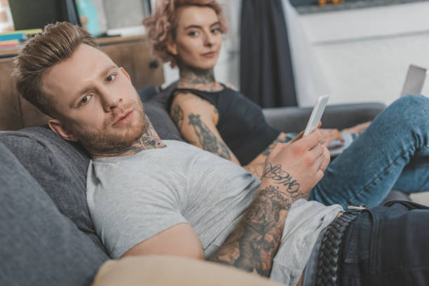 istock tattooed couple using smartphone and laptop at home 917252640