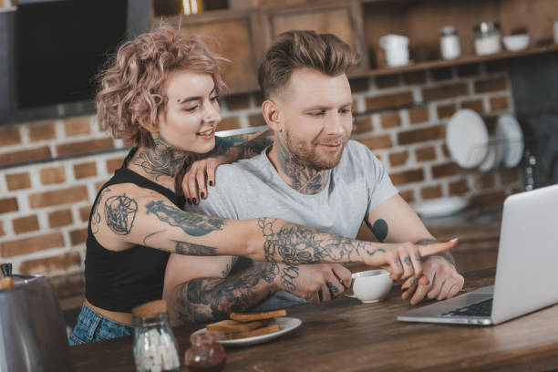 istock tattooed couple pointing at laptop during breakfast in kitchen 917252906