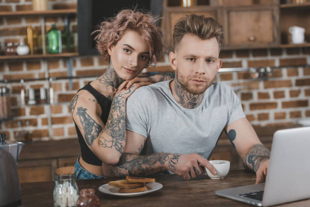 istock tattooed couple using laptop and eating breakfast in kitchen 917253116