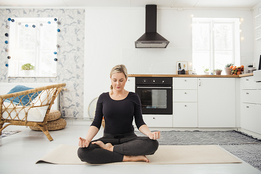 Real woman at home in kitchen doing yoga and meditation