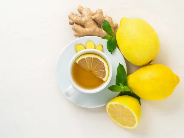 Photo of Folk ways to treat colds -  cup of tea and a slice of lemon, ginger, mint, whole lemons and half on a white background, top view.