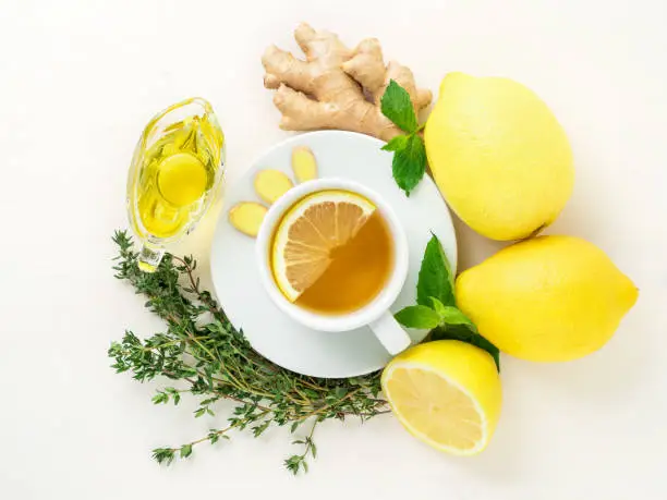 Photo of Folk ways to treat colds -  cup of tea and a slice of lemon, ginger, mint, honey, herbs, whole lemons and half on a white background, top view.