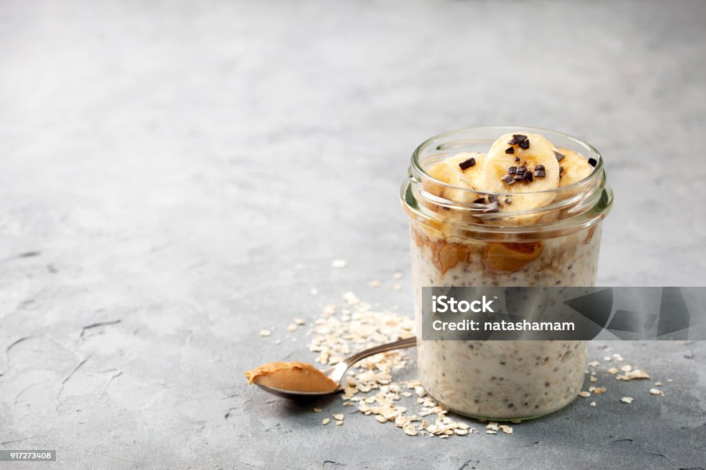 breakfast  with overnight oatmeal healthy diet breakfast. overnight oatmeal with chia seeds, bananas, peanut butter, honey, chocolate sprinkling in a glass jar on a gray concrete background Oats - Food Stock Photo