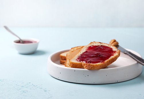 Toast with peanut butter and jam in a white ceramic plate on a blue concrete background