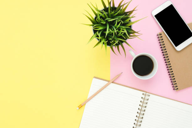 istock Office desk working space - Flat lay top view of a working space with white blank notebook page, coffee cup and mock up phone on pastel background. Pastel pink yellow color background space concept. 917277068