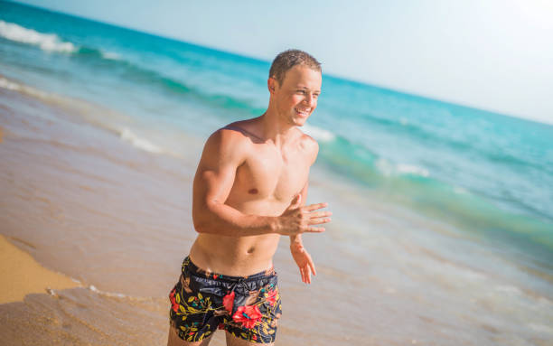 il giovane atletico ama correre su una spiaggia - men beach running shirtless foto e immagini stock