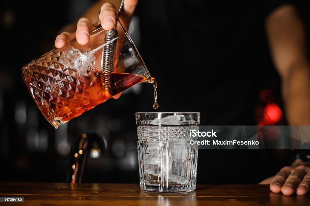 close up of bartender pouring bright red alcohol cocktail into the glass close up of bartender pouring bright red alcohol cocktail into the glass with ice Cocktail Stock Photo