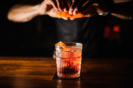 bartender with cocktail and orange peel preparing cocktail at bar. alcohol drinks, people and luxury concept