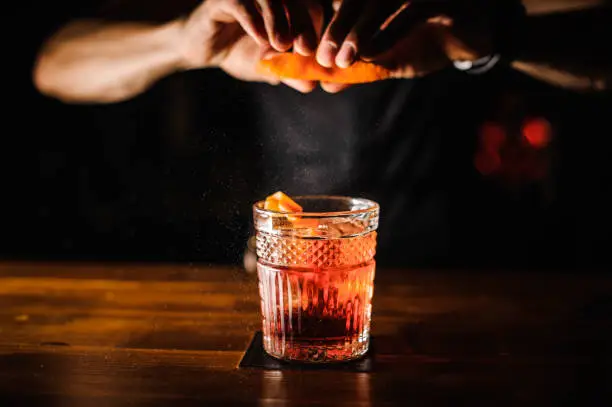 Photo of bartender with cocktail and orange peel preparing cocktail at bar