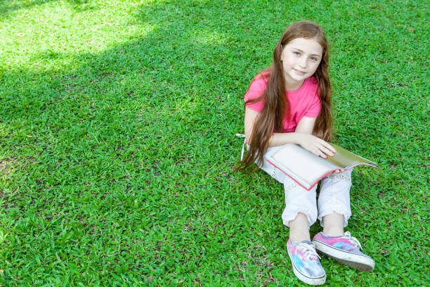 istock little gir sitting on grass and reading a book in the park 917291782