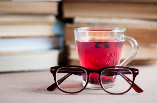 Blueberry tea in a glass cap with   eyeglasses  behind the books  background.