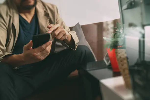 Photo of hipster hand using smart phone,digital tablet docking keyboard,coffee cup, payments online business,sitting on sofa in living room,work at home concept