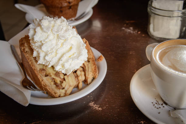 A slice of apple pie with whipped cream and a cappuccino coffee on a wooden table. A slice of apple pie with whipped cream and a cappuccino coffee on a wooden table. Landscape format. ice pie stock pictures, royalty-free photos & images