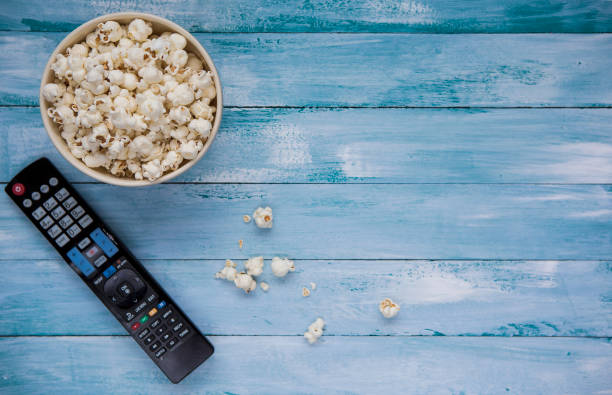 Popcorn with TV remote controler bowl with popcorn with TV remote on blue wood table remote control on table stock pictures, royalty-free photos & images