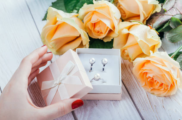 Woman opens a gift box with jewellery surrounded with roses
