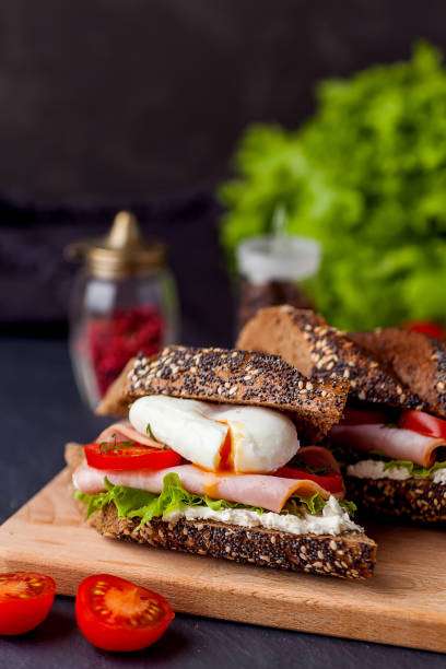 istock Sandwich with ham, poached egg and fresh tomatoes on wooden boarde. Dark background 917331802