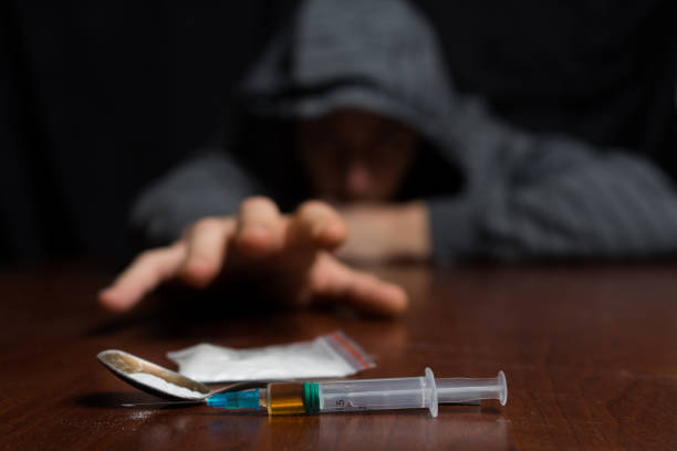 Addict at the table pulls his hand to the syringe with the dose Addict at the table pulls his hand to the syringe with the dose. Copy paste drug abuse photos stock pictures, royalty-free photos & images