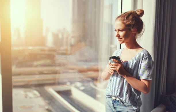 istock happy young woman drinks coffee in morning at window 917359224