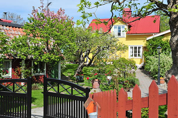 A serene garden scene featuring a rustic wooden archway surrounded by greenery and blooming flowers, including Rosa canina. A mature tree adds charm under warm sunlight.