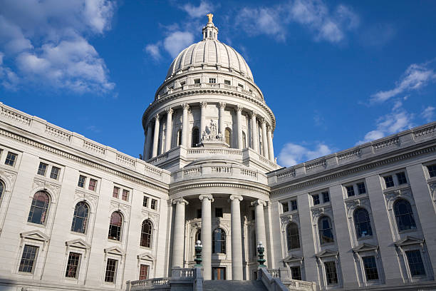 View showing USA government and business cooperation or partnerships, or the contrast of legislature and commerce, modern architecture and classical. Features historical dome of the Madison, Wisconsin state capitol building reflected in a contemporary office building steel and glass facade. Detail view under a sunny blue sky with soft clouds.
