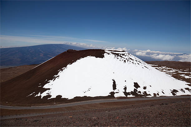 A red dirt mountain with a trail to the top at 14,000 feet overlooks the top of clouds and exposes the pink inversion layer typical of cold air environments.