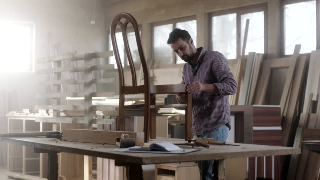 Male carpenter in furniture workshop assembling chair