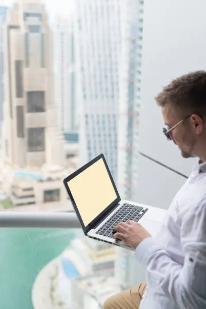 Photo of Young businessman working on his laptop, in an office with a beautiful city scape view.