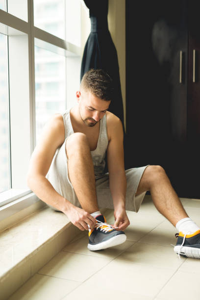istock Sportsman putting cool sneakers on, sitting next to panoramic window. 917461482