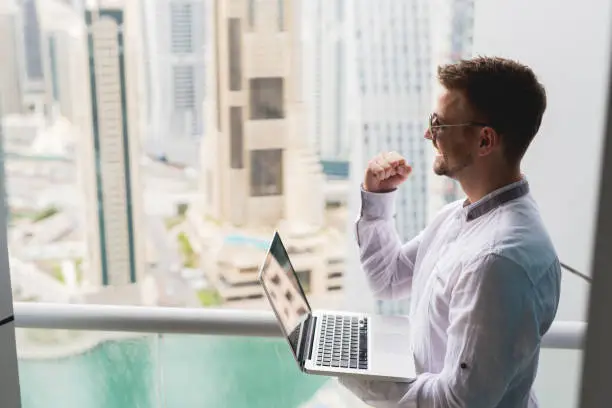 Photo of Successful businessman with panoramic city scape office view. Working laptop fist up.