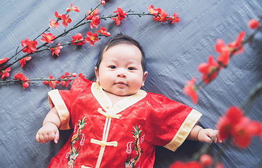 Baby in red dress on blue cloth with flower and looking. Concept Chinese New Year.