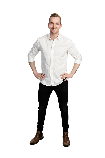 Handsome man standing in front of a white background wearing a white shirt and black jeans looking at camera.