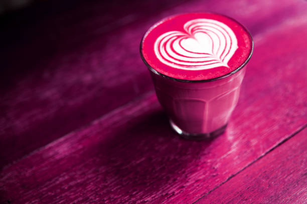 Cup of hot beetroot latte coffee is standing on the painted wooden background. Trendy healthy drink