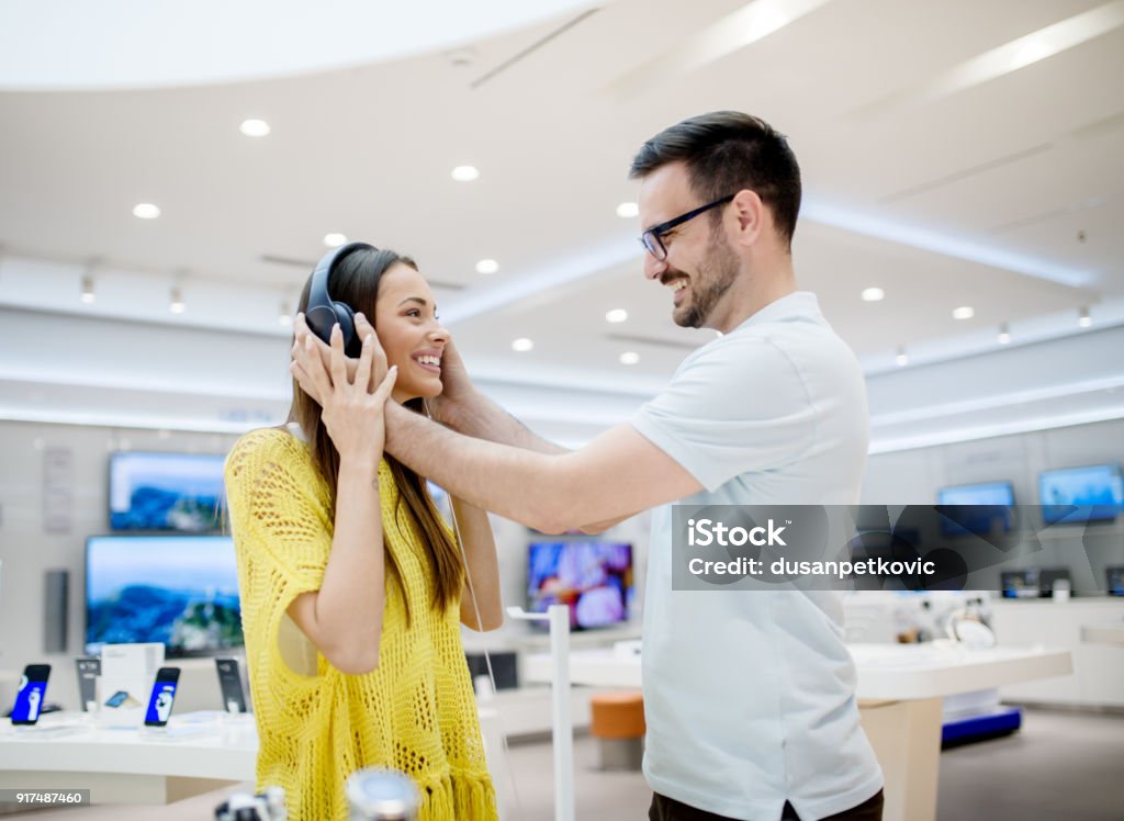 Side view of beautiful young stylish adorable love couple testing headphones in a tech store. Store Stock Photo