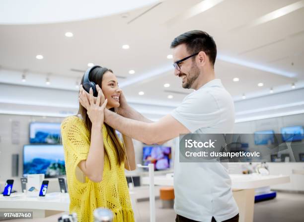 Side View Of Beautiful Young Stylish Adorable Love Couple Testing Headphones In A Tech Store Stock Photo - Download Image Now