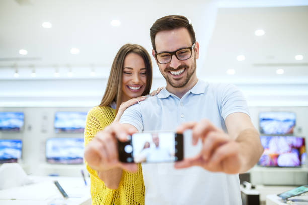 istock Charming satisfied smiling young love couple testing a mobile camera in a modern tech store. 917487536