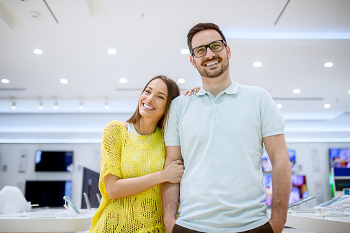 Portrait of charming young stylish adorable love couple standing hugged in a tech store.