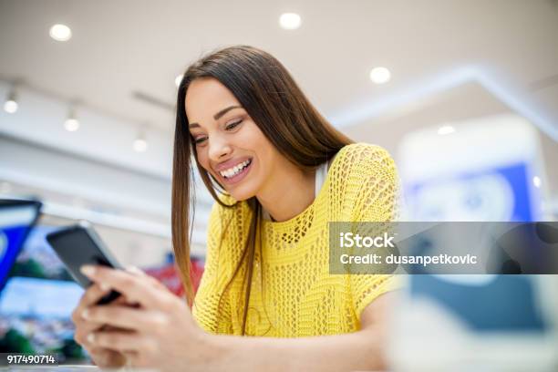 Close Up View Of Satisfied Young Smiling Attractive Brunette Girl Testing Mobile In A Tech Store Stock Photo - Download Image Now