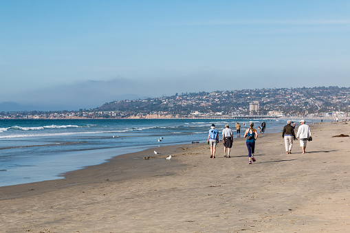 San Diego, California - February 9, 2018:  People walk on Mission Beach, a beach of just over one mile in length and one of the most popular beaches in the area.  It is adjacent to Belmont Park.