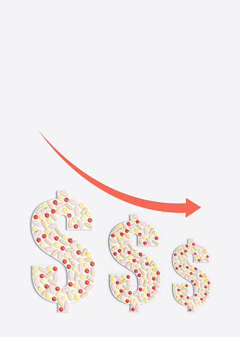 A shot from above of three cut out paper dollar sign in the center with various pills of different colors arranged on the top of them on the white background. A red arrow shows an downward trend.
