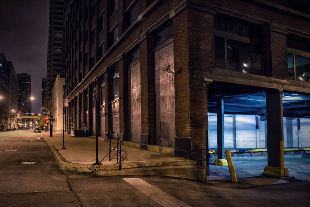 esquina de rua no centro de cidade escura com um carregamento de armazém industrial atracar durante a noite. - abandoned city street built structure - fotografias e filmes do acervo