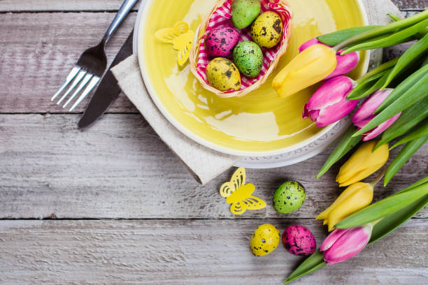 Easter table setting with spring tulips, colorful quail eggs and cutlery on shabby wooden table. Holidays Spring Background. Top view, flat lay, copy space