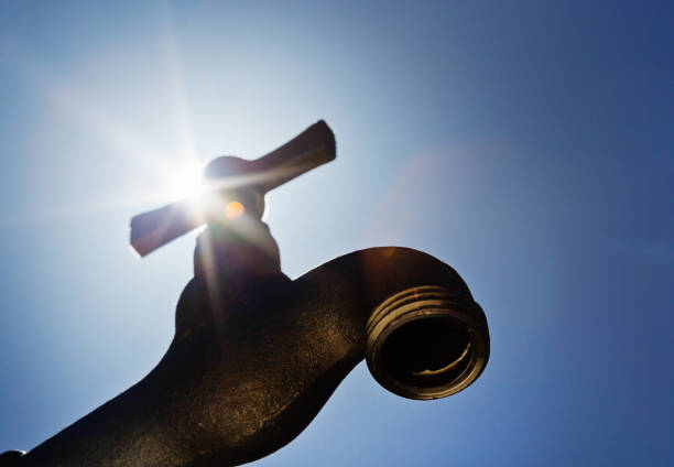 Hot sun blazes above a dry faucet, symbolizing drought.