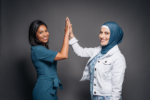 Portrait of authentic, real, beautiful people. Studio shot of Brazilian woman in dark green formal businesswear - elegant dress with her friend from Middle East who is wearing headscarf.