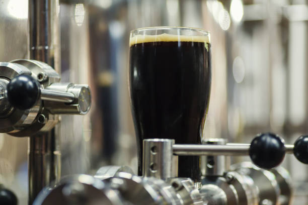 Pint glass of dark stout beer standing on brewing equipment in an operating brewery