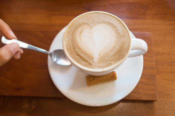 Hot white ceramic coffee cup with heart shape latte art on wooden background