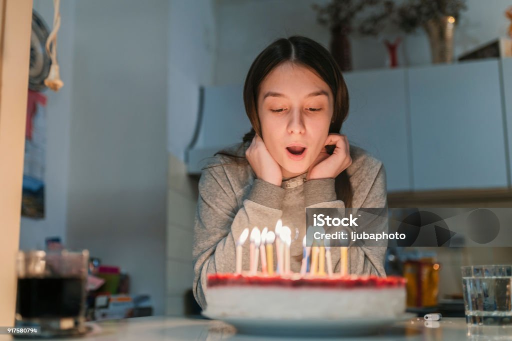 It's my birthday! Happy little girl celebrating her birthday and blowing candles on homemade baked cake, indoor. Birthday party for children. Carefree childhood, anniversary, happiness. Pretty beautiful caucasian Teenage Girl Blowing Birthday Cake Candles Birthday Stock Photo