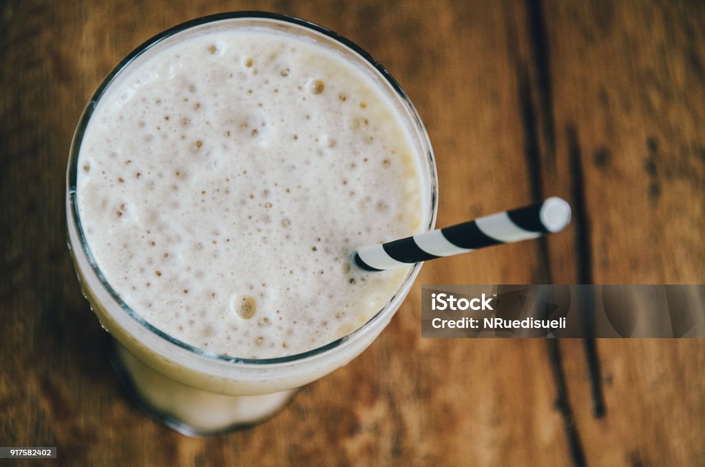 Frothy ice coffee in glass with drinking straw on wooden background, top view close up Milkshake Stock Photo