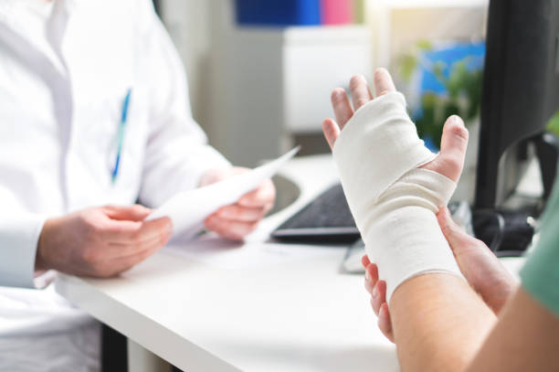 Injured patient showing doctor broken wrist and arm with bandage in hospital office or emergency room. Sprain, stress fracture or repetitive strain injury in hand. Injured patient showing doctor broken wrist and arm with bandage in hospital office or emergency room. Sprain, stress fracture or repetitive strain injury in hand. Nurse helping customer. First aid. sprain stock pictures, royalty-free photos & images