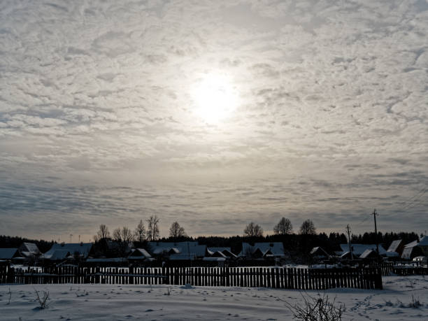 Sun lighting through clouds in the sky over winter village covered with snow